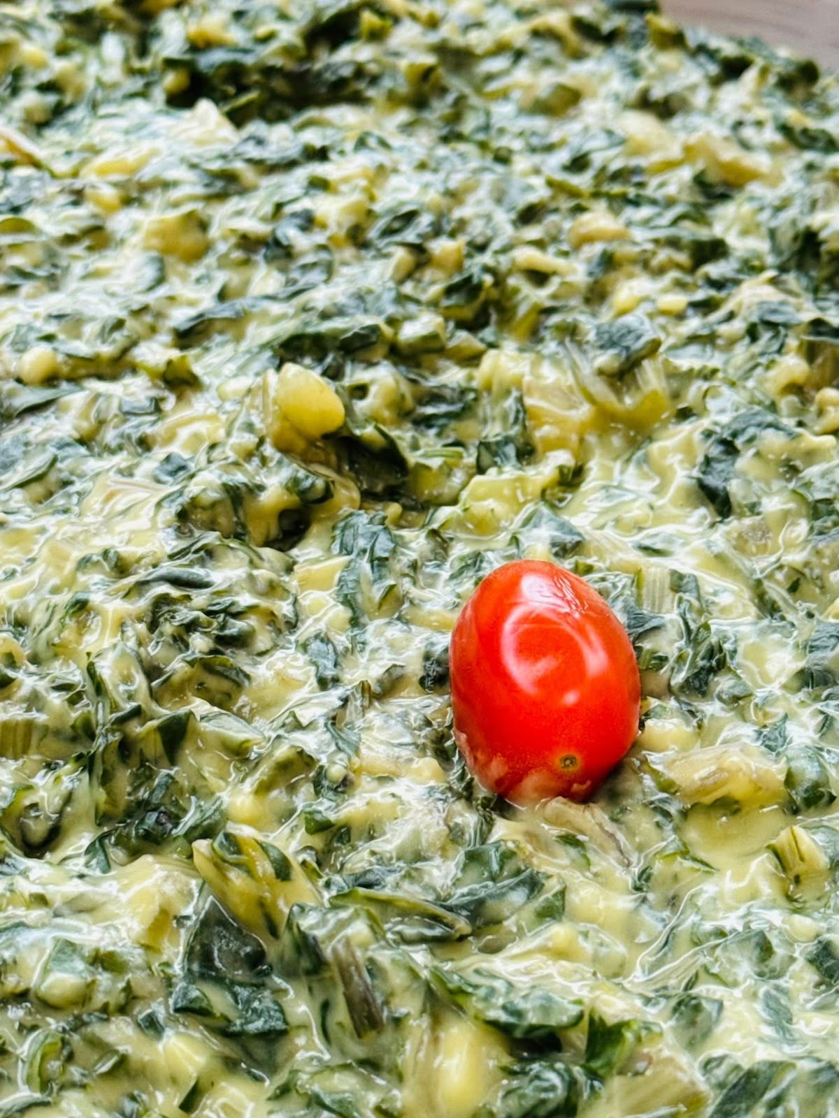Creamed spinach side dish garnished with a cherry tomato