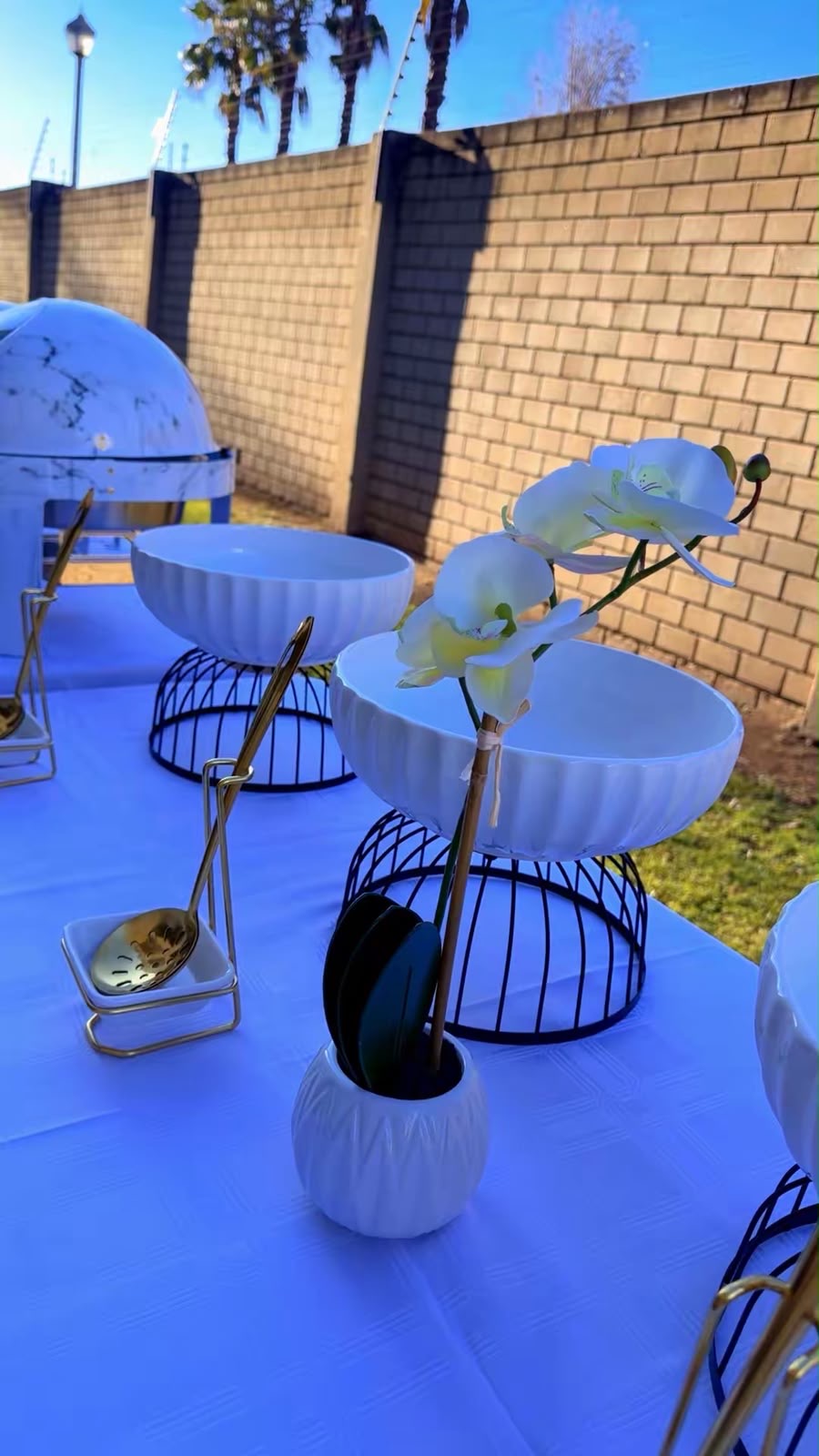 White salad bowls on black stands with gold serving spoons